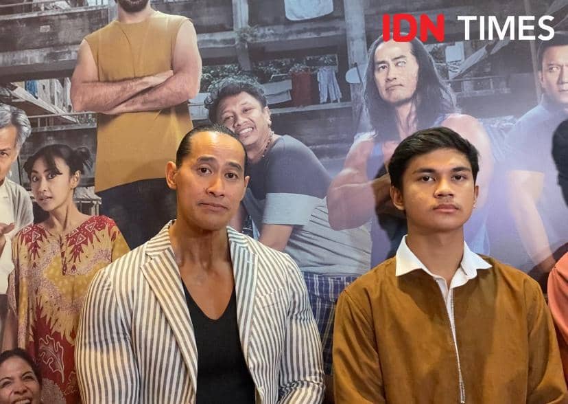 Ade Rai berpose bersama seorang pria muda di acara press screening film Semua Akan Baik-Baik Saja dengan latar poster film di belakang mereka.