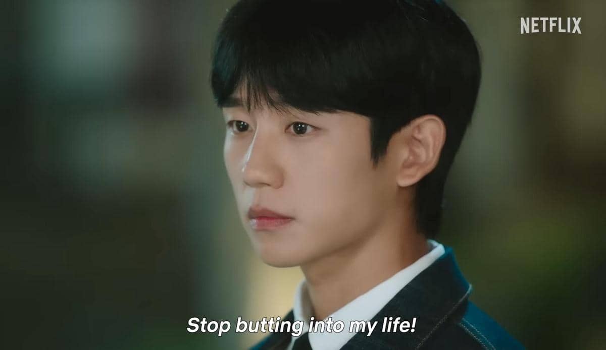 Seorang pria muda berwajah serius mengenakan jas gelap dan kemeja putih dalam adegan serial Love Next Door di Netflix.