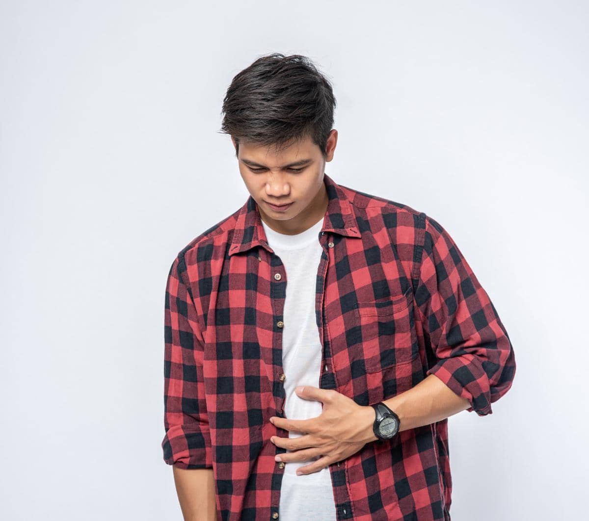 Seorang pria mengenakan kemeja kotak-kotak merah hitam memegang perutnya sambil menunduk dengan ekspresi lapar di latar putih.