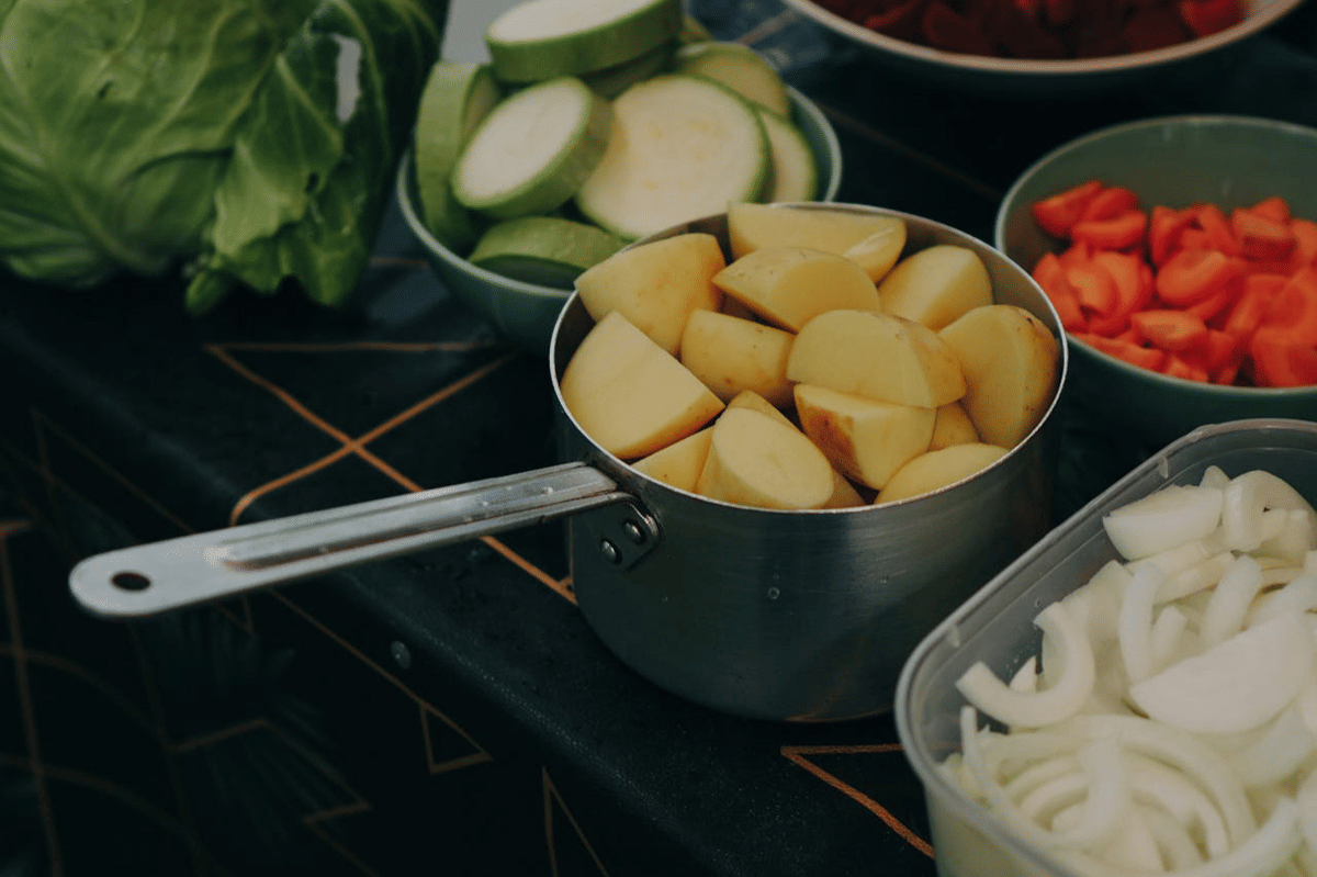 Potongan kentang, bawang bombai, wortel, dan zucchini disiapkan dalam wadah di atas meja dapur sebagai bahan membuat ragout.