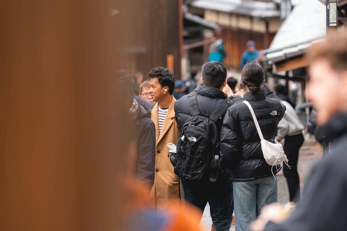 Sekelompok orang berjalan di jalan sempit dengan bangunan kayu tradisional di Jepang pada suasana musim dingin yang ramai.