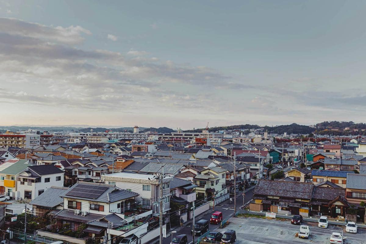 Pemandangan kota di Jepang dengan deretan rumah tradisional dan modern di bawah langit sore yang berawan lembut.