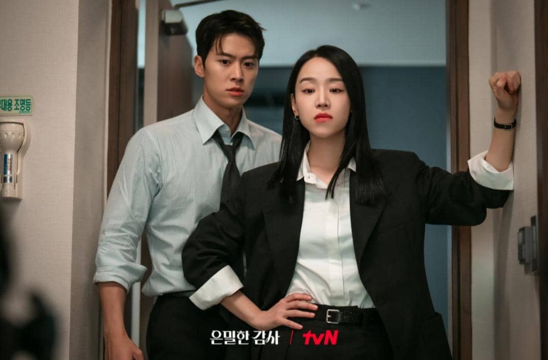 Dua pemeran utama drama Korea Filing for Love berdiri di depan pintu dengan ekspresi serius mengenakan pakaian formal.