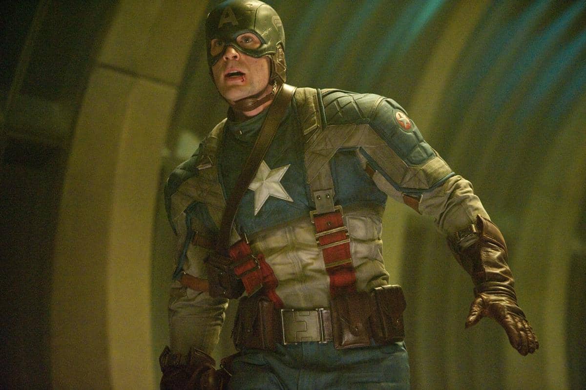 Captain America mengenakan kostum biru dengan bintang putih di dada dan sabuk perlengkapan, berdiri di dalam ruangan bercahaya kuning kehijauan.