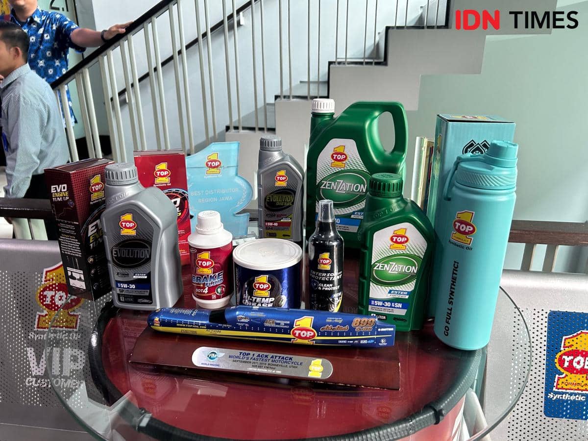 Beragam produk pelumas TOP 1 seperti oli mesin, cairan rem, dan aditif kendaraan tersusun di atas meja kaca di area dalam ruangan.