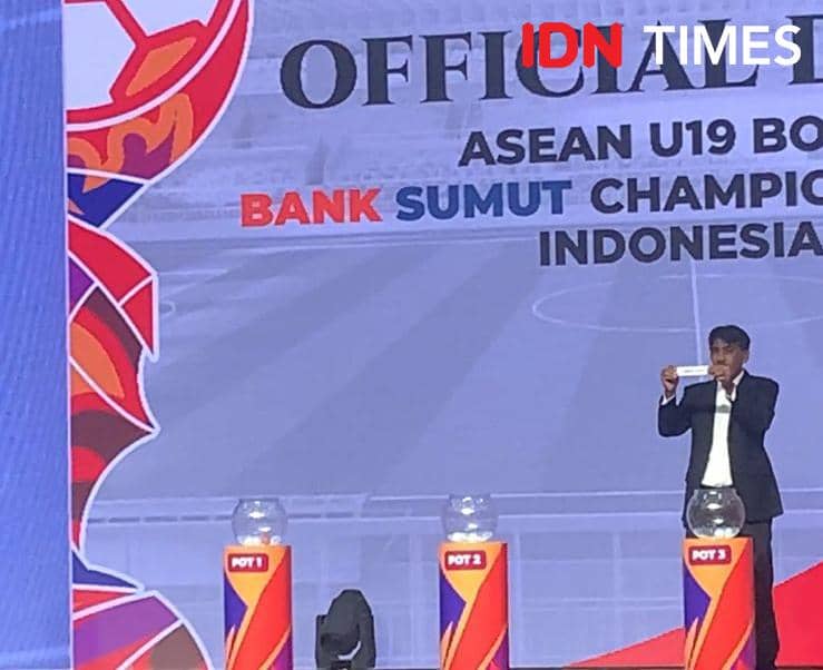 Seorang pria mengenakan jas hitam menarik undian Piala AFF U-19 di atas panggung dengan latar tulisan resmi turnamen di Medan.