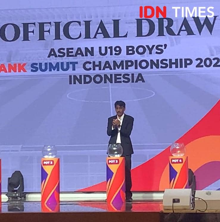 Seorang pria berdiri di panggung acara undian resmi Piala AFF U-19 2026 di Medan dengan latar tulisan ASEAN U19 Boys Championship Indonesia.