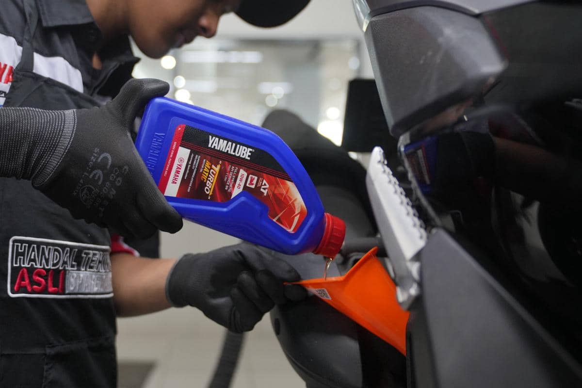 Seorang teknisi menuangkan oli Yamalube ke mesin motor menggunakan corong oranye saat proses penggantian oli di bengkel.