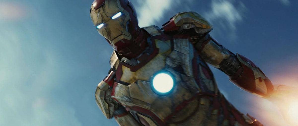 Karakter Iron Man mengenakan baju zirah merah dan emas dengan reaktor bercahaya di dada, terbang di langit biru.