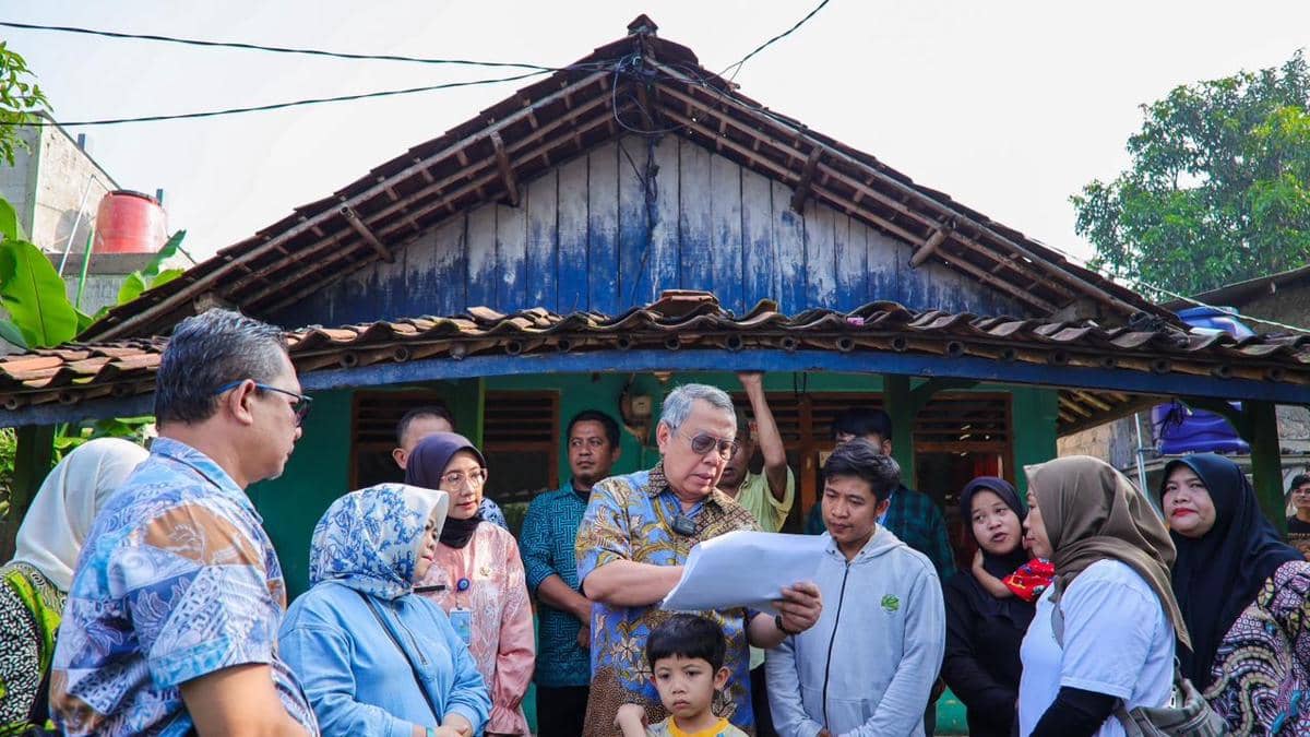 Sejumlah pejabat dan warga berdiskusi di depan rumah sederhana dengan cat biru yang tampak usang di Tangerang Selatan.