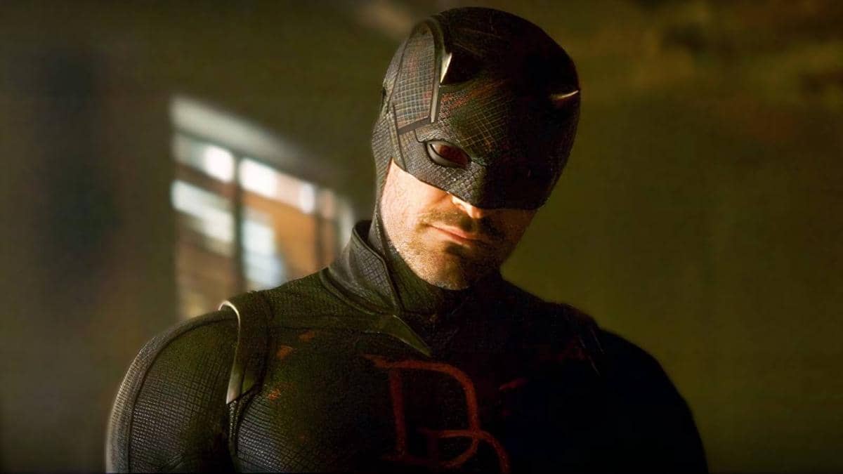 Karakter Daredevil mengenakan kostum hitam dengan simbol merah di dada, berdiri di ruangan bercahaya redup.