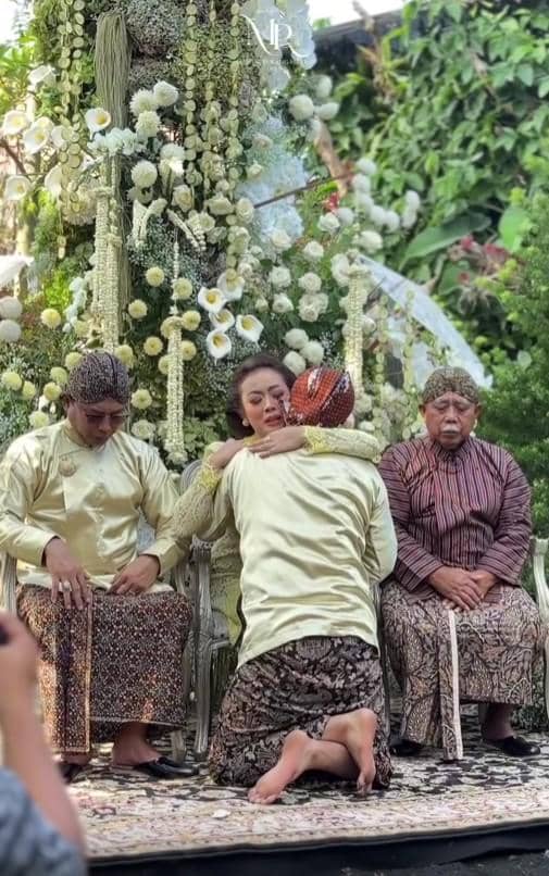 Momen haru prosesi sungkeman dalam acara siraman adat Jawa dengan dekorasi bunga putih dan keluarga mengenakan busana tradisional.