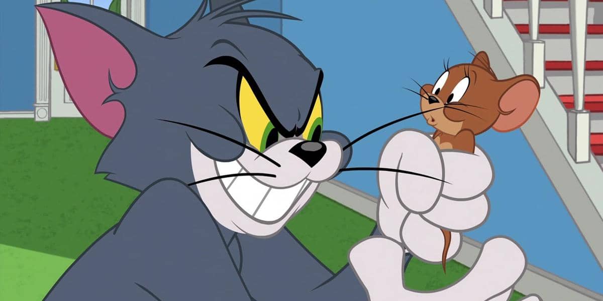 Tom si kucing abu-abu memegang Jerry si tikus cokelat kecil dengan ekspresi licik di dalam rumah berwarna cerah.