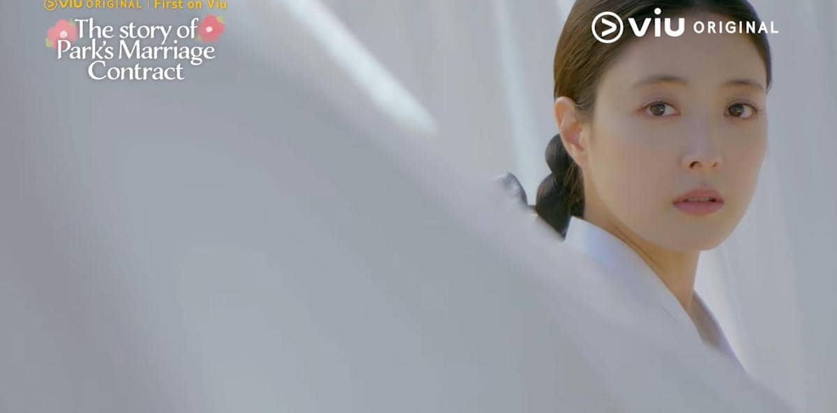 Seorang wanita mengenakan hanbok putih menatap ke arah kamera dalam cuplikan drama The Story of Park's Marriage Contract di Viu.