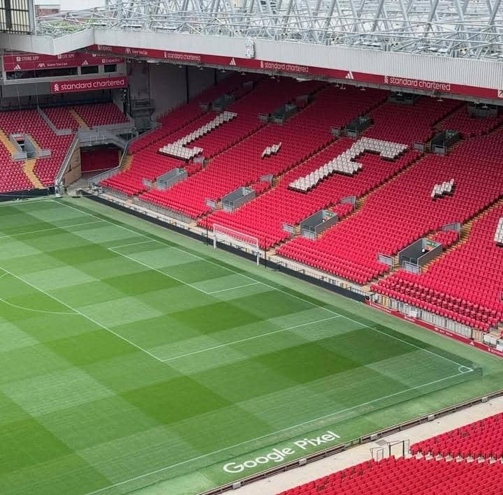 Pemandangan tribun Stadion Anfield dengan kursi merah bertuliskan L.F.C. dan lapangan hijau yang terawat rapi.