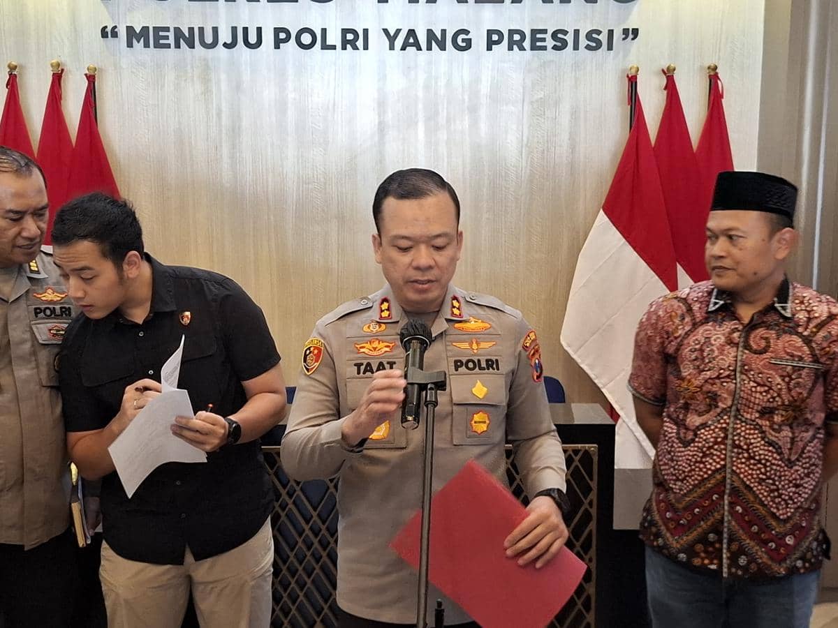 Seorang perwira polisi berbicara di depan mikrofon didampingi beberapa orang di ruangan dengan latar bendera merah putih dan tulisan menuju Polri yang presisi.