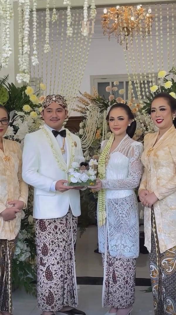 Pasangan pengantin mengenakan busana adat Jawa berwarna putih dan batik saat prosesi akad pernikahan dengan dekorasi bunga melati.