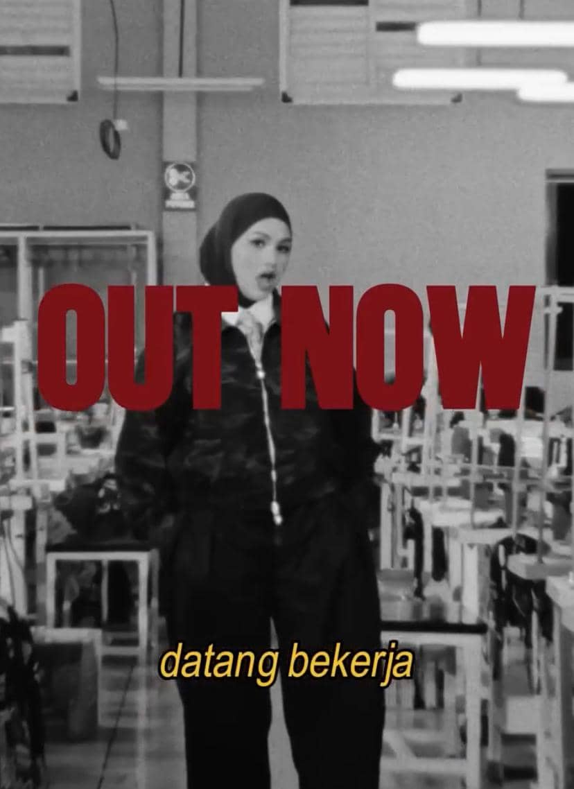 Seorang perempuan berhijab berdiri di dalam ruangan pabrik dengan tulisan besar 'OUT NOW' dan teks kecil 'datang bekerja' di bagian bawah.