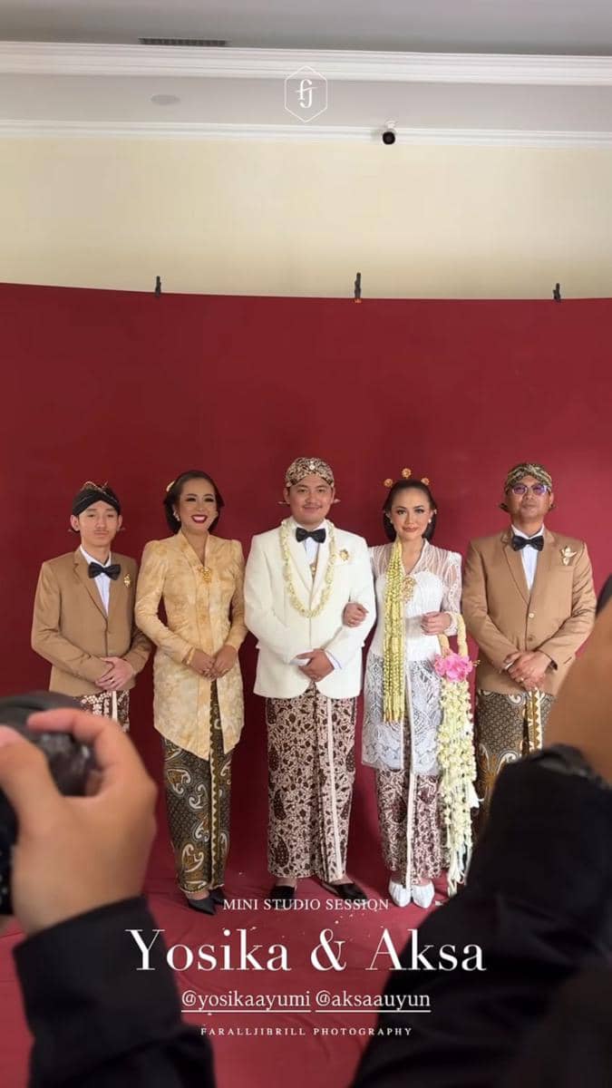 Lima orang berpose dalam busana adat Jawa di depan latar merah saat sesi foto pernikahan, dua di antaranya adalah pengantin.