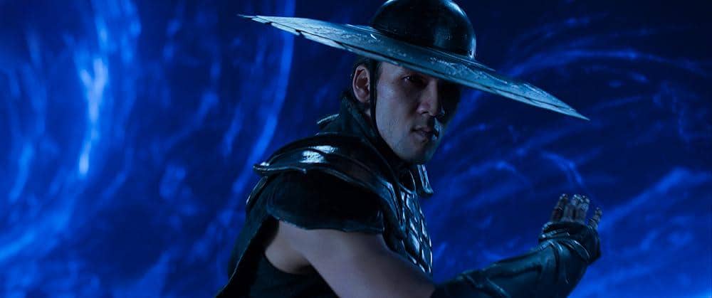 Seorang karakter mengenakan topi logam lebar dan pakaian tempur gelap bersiap bertarung di latar biru bercahaya dalam film Mortal Kombat 2.