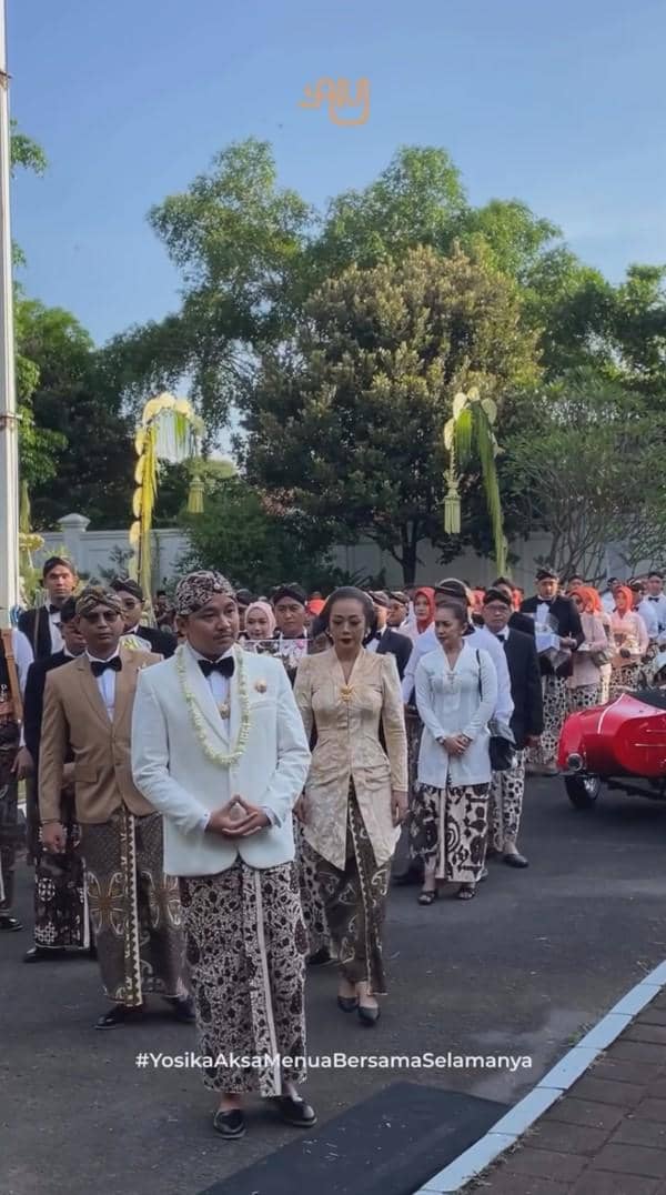 Prosesi akad pernikahan adat Jawa dengan pengantin pria mengenakan beskap putih dan pengantin wanita berkebaya krem diikuti rombongan keluarga.