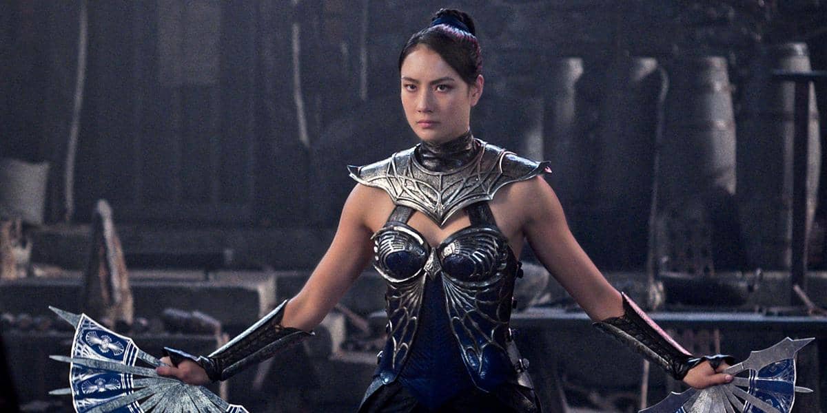 Seorang karakter perempuan mengenakan baju zirah logam dan memegang dua kipas tajam di latar gelap dalam adegan film Mortal Kombat 2.