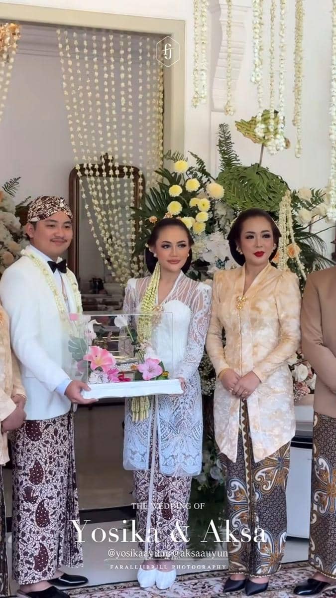 Pasangan pengantin mengenakan busana adat Jawa berpose bersama keluarga di acara akad pernikahan dengan dekorasi bunga melati dan nuansa putih.