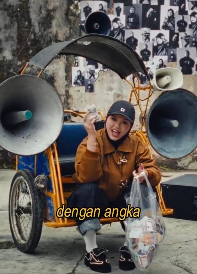 Seorang perempuan mengenakan jaket cokelat dan topi hitam duduk di becak dengan pengeras suara besar, memegang kantong plastik berisi uang.