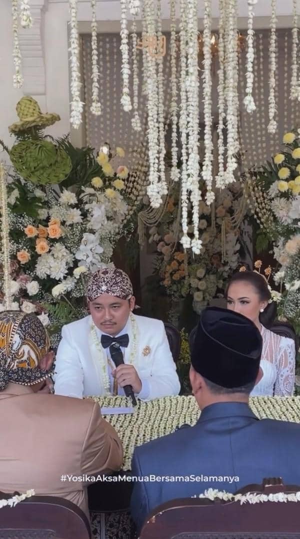 Pasangan pengantin duduk di depan penghulu saat prosesi akad nikah dengan dekorasi bunga dan janur melati yang indah.