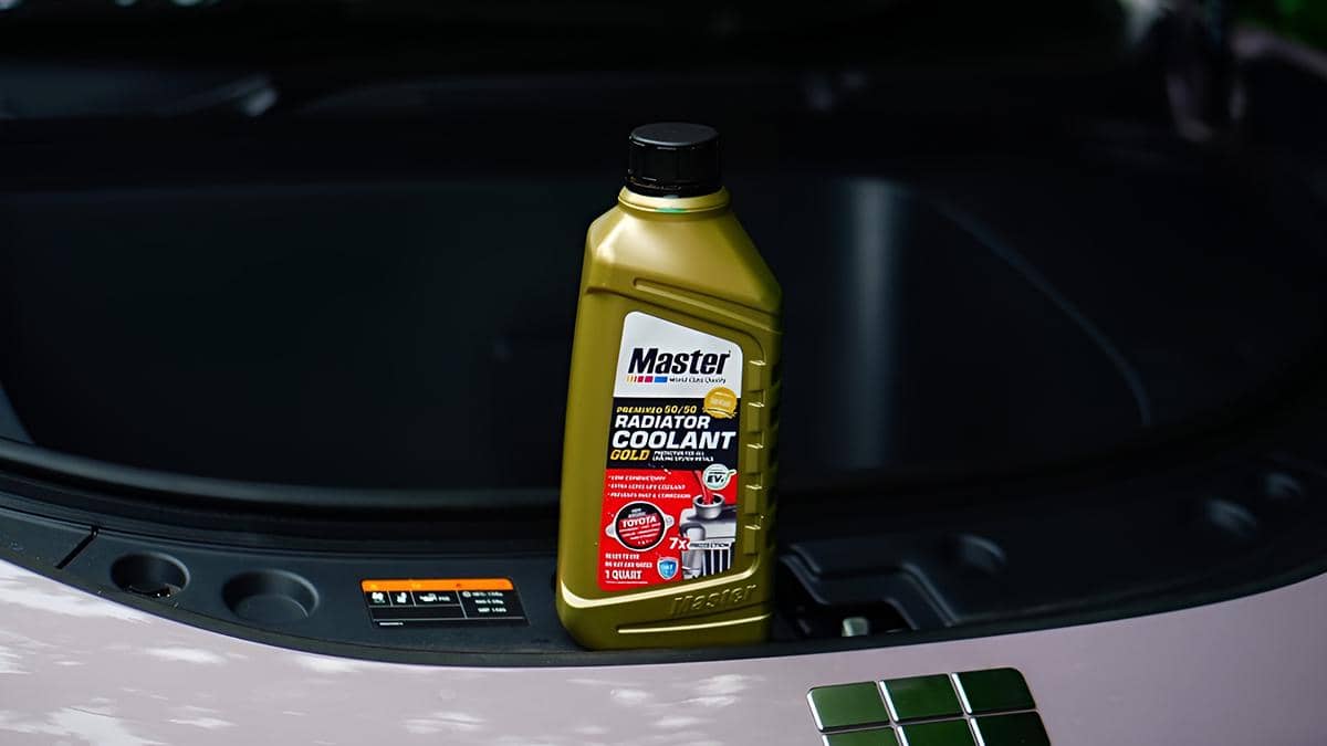 Botol cairan radiator Master Radiator Coolant Gold ditempatkan di ruang mesin mobil dengan latar belakang gelap.