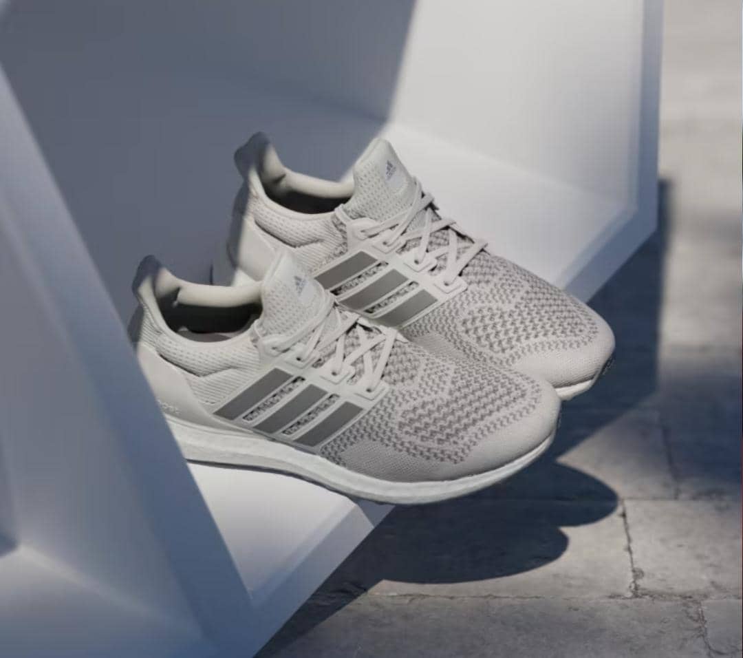 Sepasang sepatu lari Adidas Ultraboost 1.0 berwarna abu-abu muda dengan desain rajutan halus dan sol tebal berwarna putih.