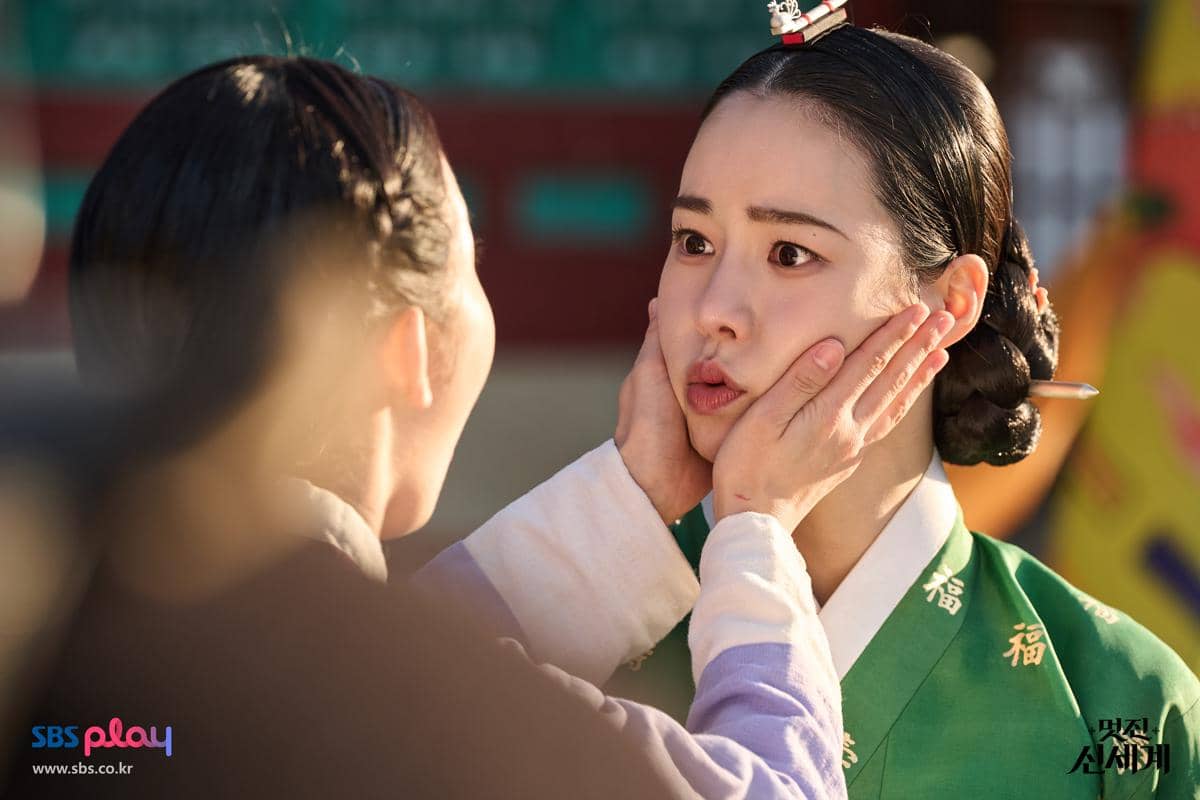 Dua perempuan dalam balutan hanbok tradisional Korea, salah satunya memegang pipi yang lain dengan ekspresi terkejut di adegan drama My Royal Nemesis.