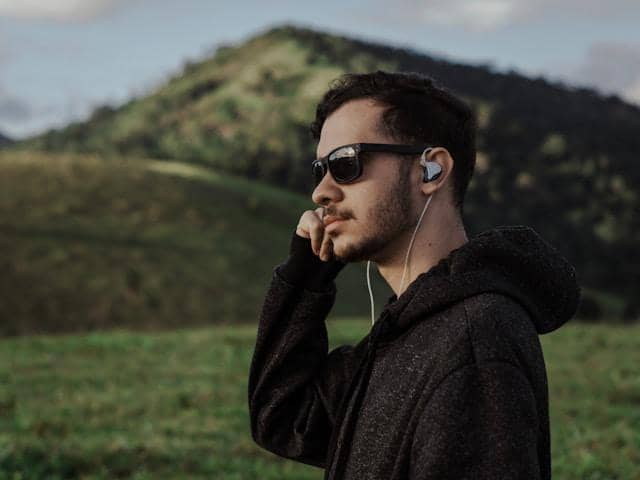 pengguna memakai earphone kabel sambil menikmati pemandangan pegunungan