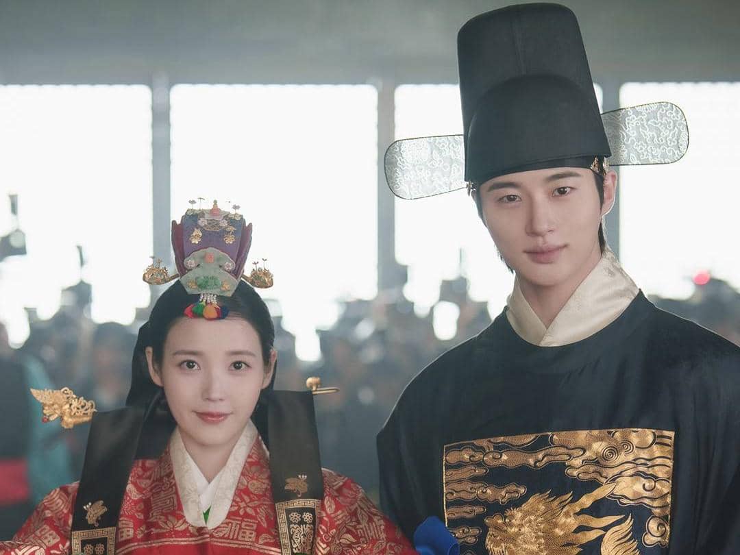 Dua aktor mengenakan hanbok kerajaan tradisional Korea dalam adegan drama sejarah Perfect Crown dengan latar istana.