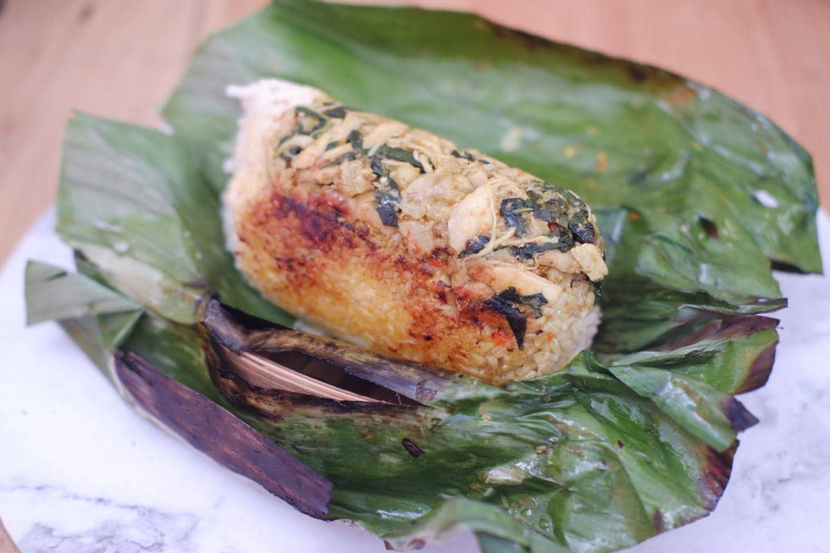 Nasi bakar berisi ayam suwir dan bumbu rempah dibungkus daun pisang, tampak hangat dengan bagian luar sedikit gosong.