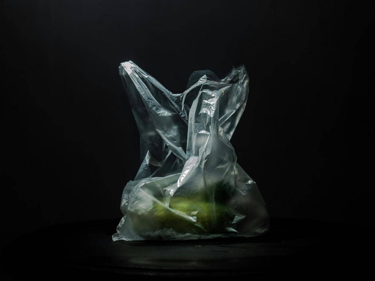 Kantong plastik sekali pakai transparan berisi beberapa buah berwarna hijau dengan latar belakang gelap.