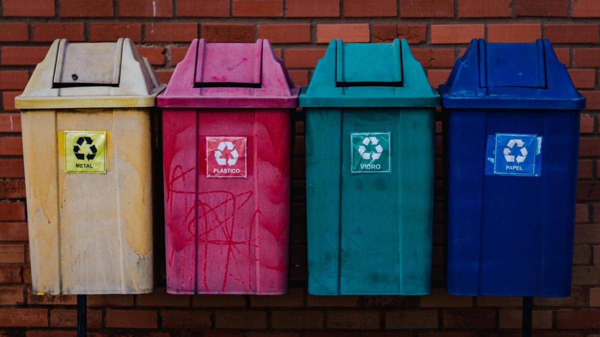  Empat tempat sampah daur ulang berwarna berbeda untuk metal, plastik, kaca, dan kertas di depan dinding bata