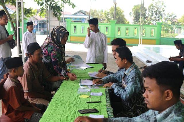 Beberapa santri dan orang dewasa duduk di meja panjang berwarna hijau, melakukan kegiatan administrasi di lingkungan pesantren.