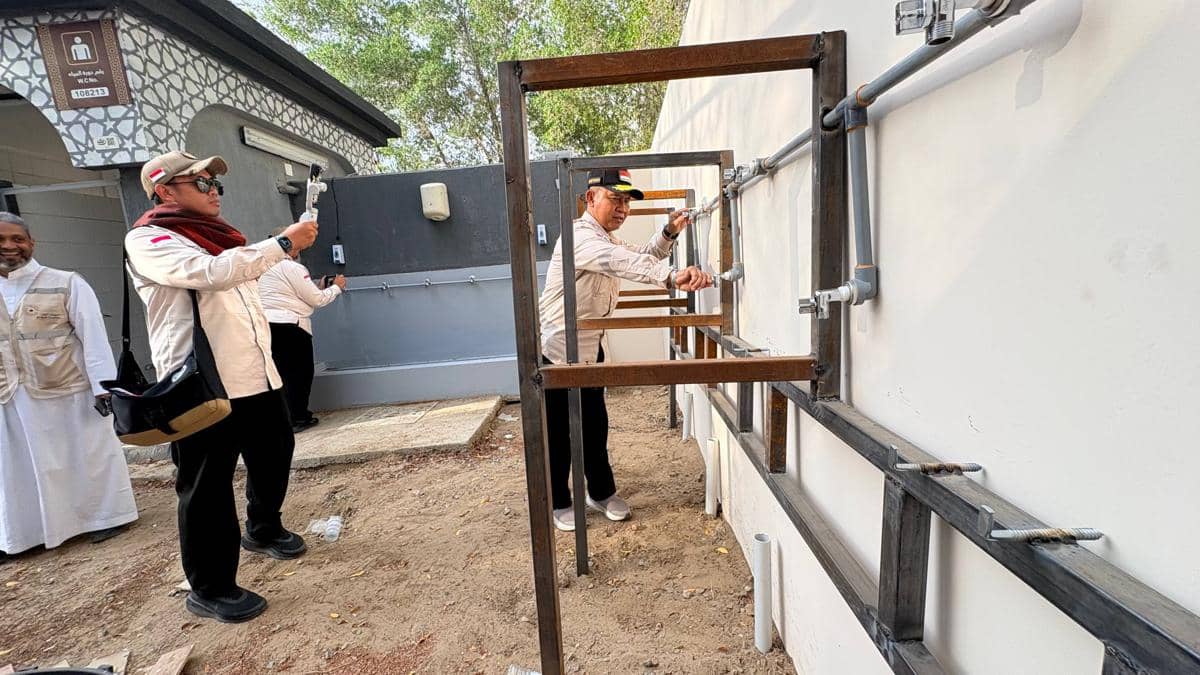 Petugas Kementerian Agama memeriksa instalasi pipa dan rangka fasilitas tenda jemaah haji Indonesia di area luar bangunan.