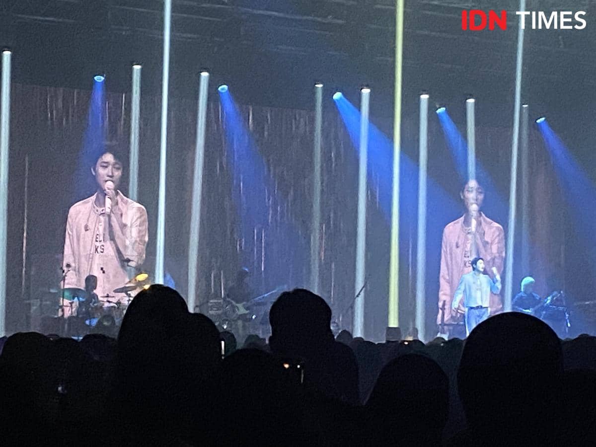 Penyanyi tampil di atas panggung dengan pencahayaan biru dan kuning di konser WOODZ di The Kasablanka, Jakarta, disaksikan banyak penonton.