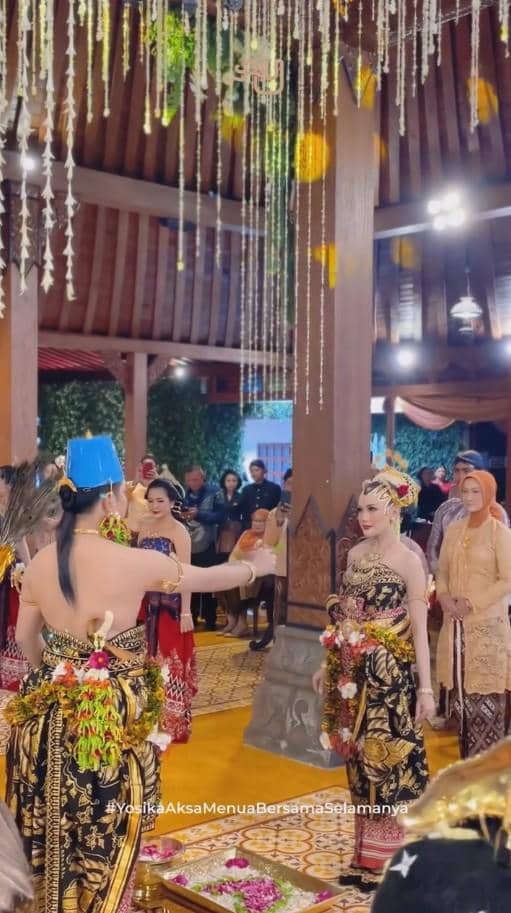 Prosesi ngunduh mantu dengan pengantin dan penari mengenakan busana adat Jawa di pendopo berhias janur dan bunga gantung.