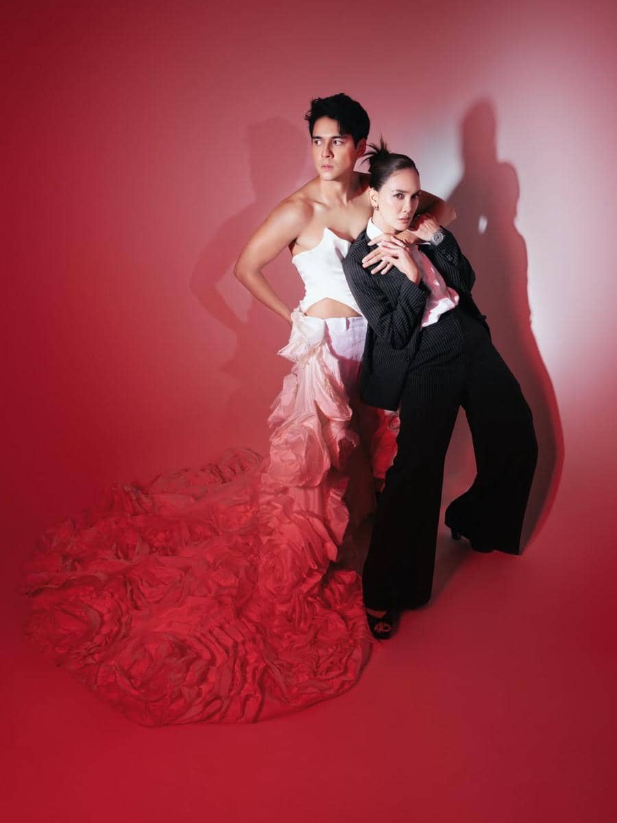 Dua model berpose dalam pemotretan artistik dengan pencahayaan merah, satu mengenakan gaun panjang bertekstur dan satu mengenakan setelan hitam.