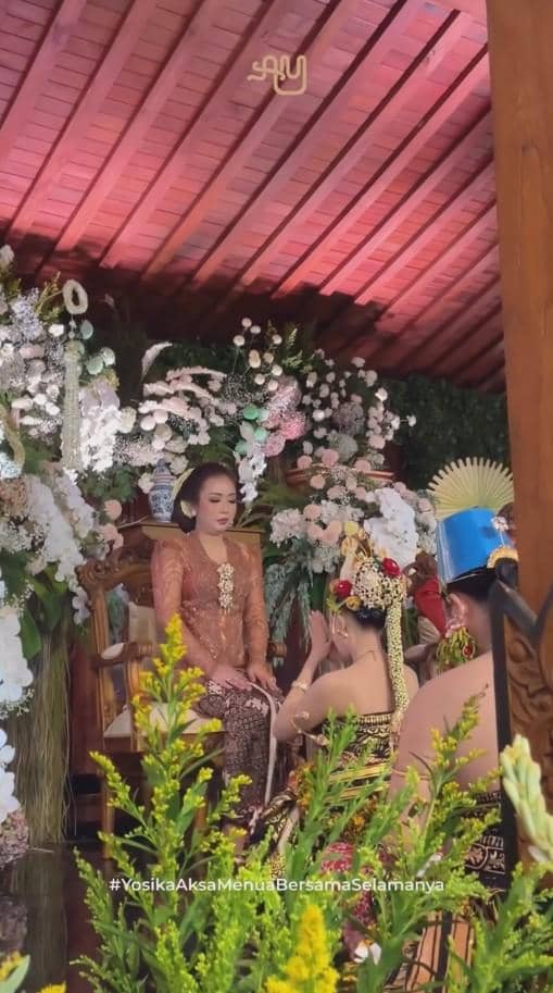 Prosesi ngunduh mantu dengan pengantin mengenakan busana adat Jawa, dikelilingi dekorasi bunga dan nuansa tradisional di pendopo.