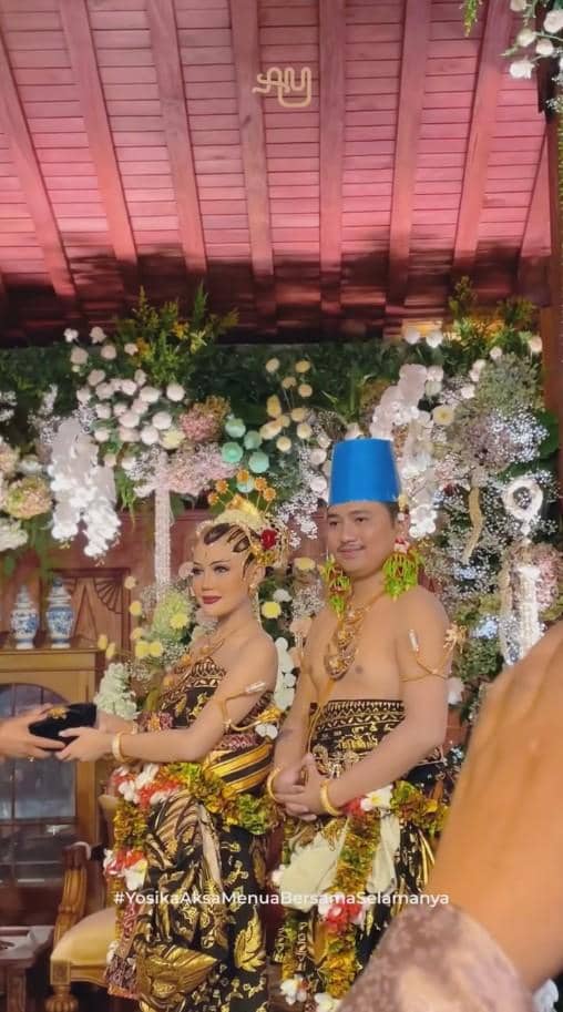 Pasangan pengantin mengenakan busana adat Jawa dengan hiasan bunga dan ornamen tradisional saat acara ngunduh mantu di pendopo.