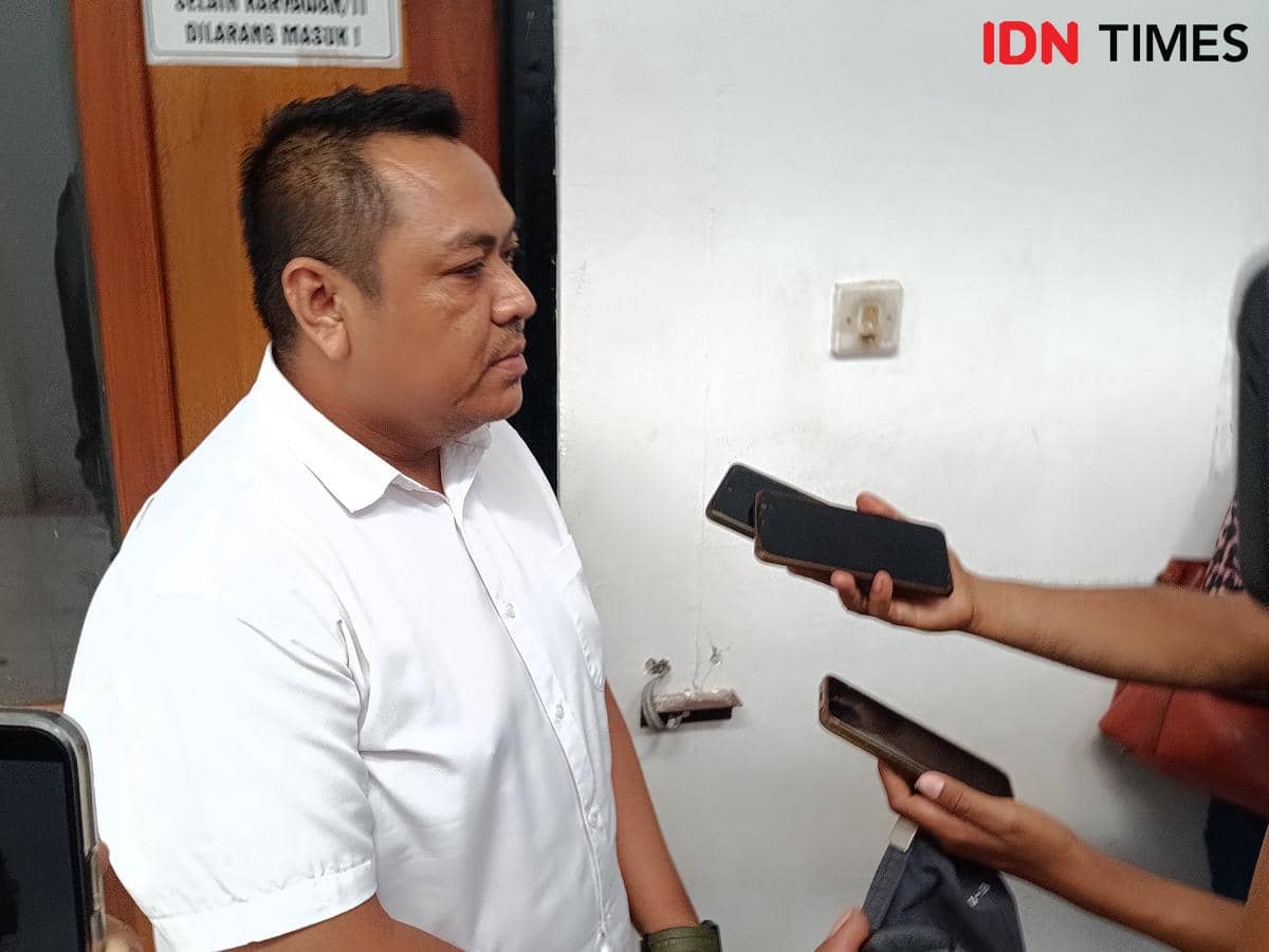 Seorang pria mengenakan kemeja putih diwawancarai oleh beberapa jurnalis yang memegang ponsel di depan ruang sidang Pengadilan Negeri Kupang.