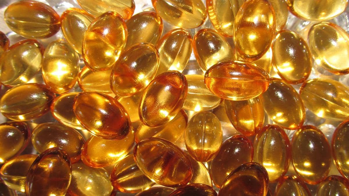 Kapsul vitamin E berwarna kuning keemasan dengan bentuk oval transparan yang tampak berkilau di bawah cahaya.