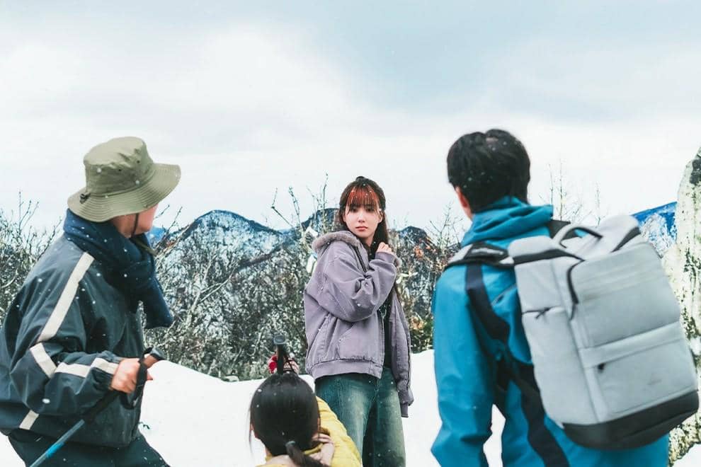 Empat orang berdiri di area bersalju dengan latar pegunungan, mengenakan pakaian musim dingin dan tampak berbincang di tengah salju.