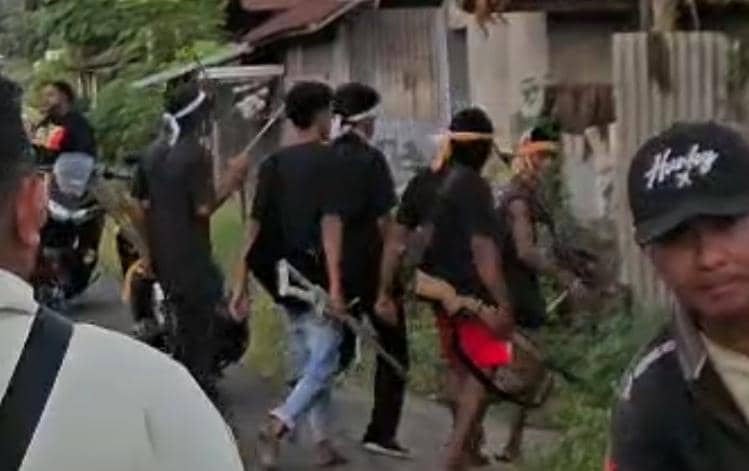 Sekelompok warga di Adonara Timur berjalan di jalan desa sambil membawa senapan rakitan dan mengenakan ikat kepala berwarna putih dan oranye.