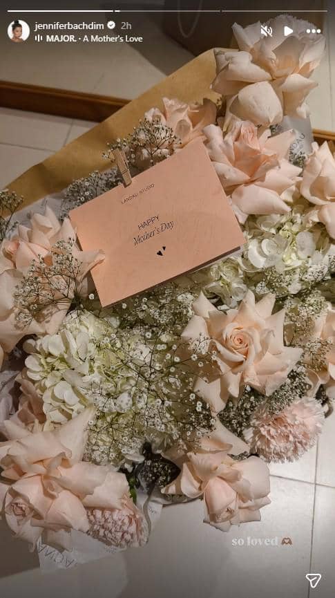 Karangan bunga berisi mawar dan bunga putih dengan kartu ucapan bertuliskan Happy Mother’s Day di atasnya.