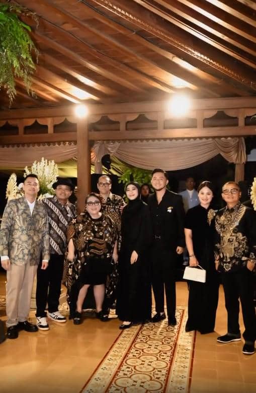 Sekelompok tamu mengenakan busana formal dan batik berfoto bersama di resepsi pernikahan dengan latar dekorasi tradisional Jawa.
